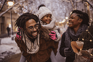 Walking down a snowy street, a black family smiles and embraces in winter.